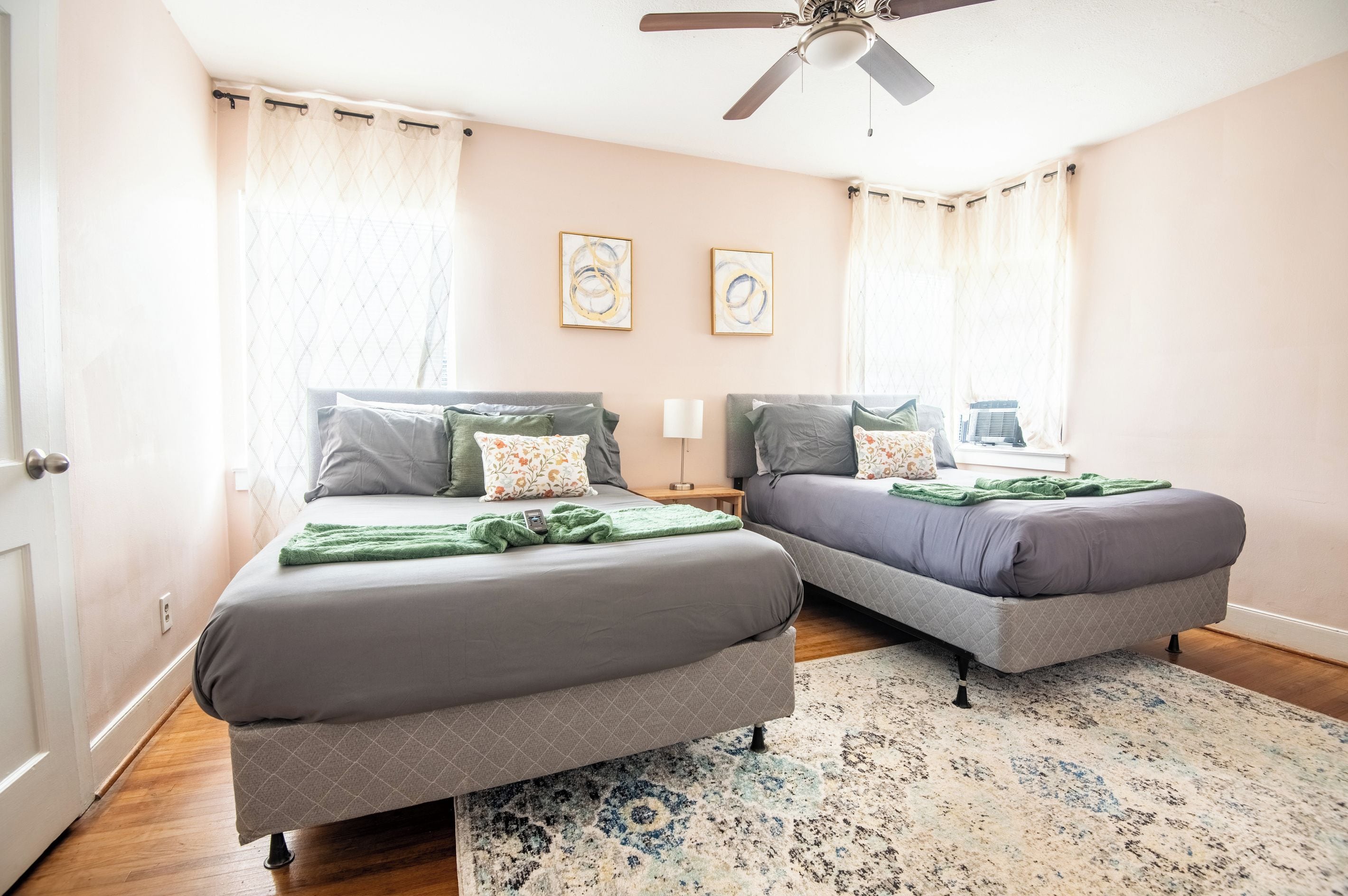 Une chambre avec deux lits, un ventilateur de plafond et un tapis à motifs.