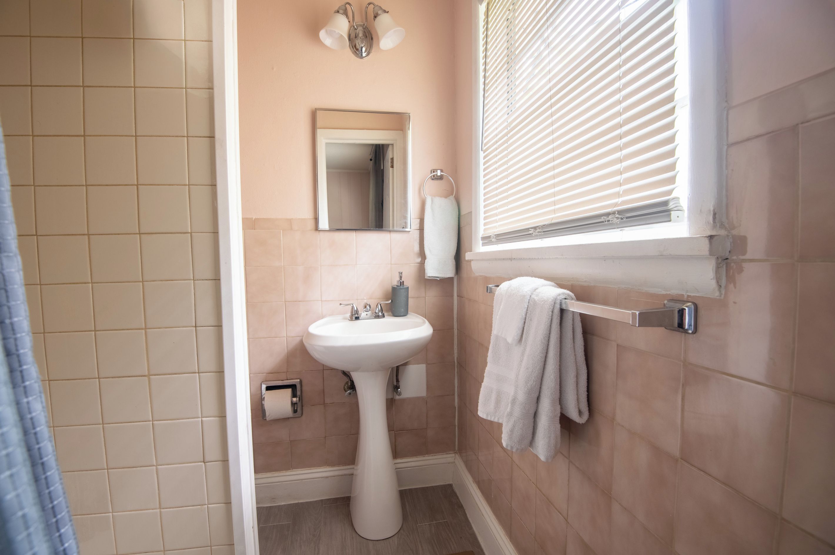 A bathroom with a sink, mirror, towel rack, and window with blinds.