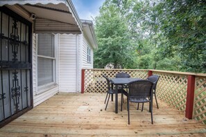 A wooden deck with a table and chairs, a lattice fence, and a house with a white exterior and black window grills.
