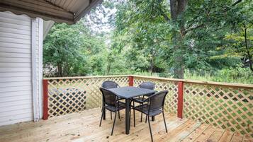 A wooden deck with a table and chairs, surrounded by a wooden fence and trees.