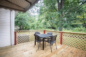 A wooden deck with a table and chairs, surrounded by a wooden fence and trees.
