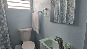 Une salle de bain avec des toilettes, un lavabo et une fenêtre avec des stores.