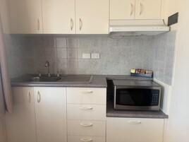 Una cocina compacta con microondas integrado, un lavamanos y un escurreplatos.