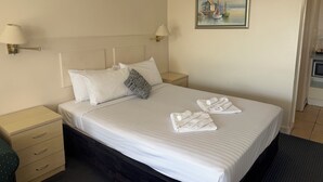 Una habitación de hotel con cama, dos mesitas de noche, aire acondicionado instalado en la pared y un cuadro.