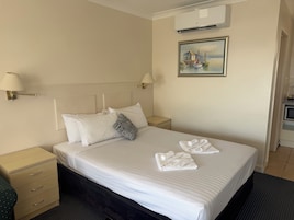 Una habitación de hotel con cama, dos mesitas de noche, aire acondicionado instalado en la pared y un cuadro.