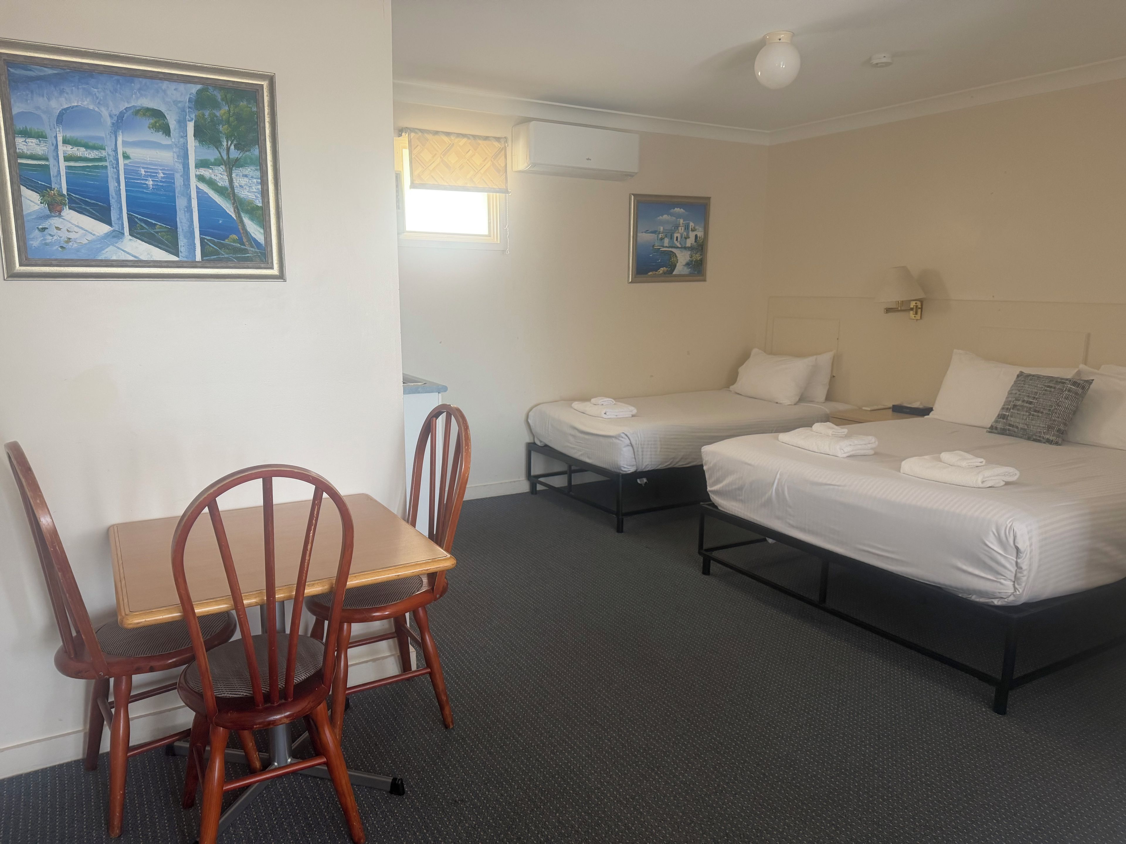 Habitación de hotel con cama, escritorio y silla. Hay dos camas, una más grande y otra más pequeña.