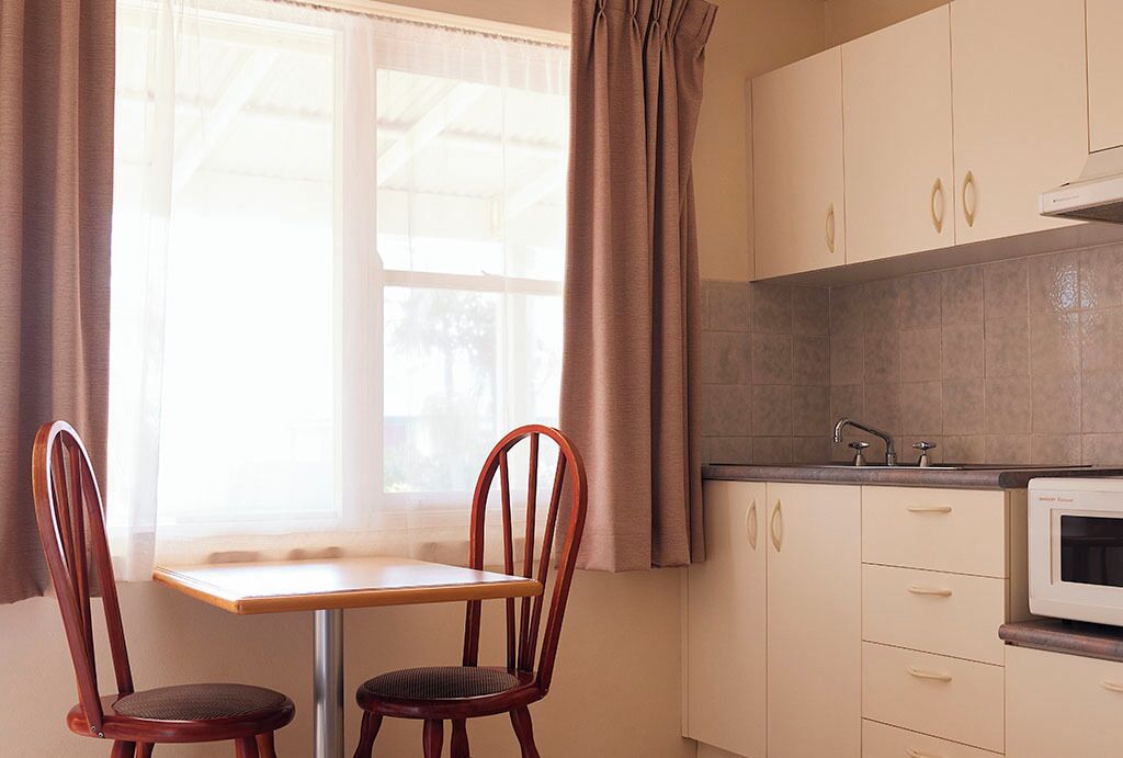 A kitchen with a window, two wooden chairs, a table, and a microwave.