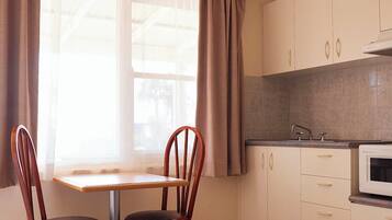 A kitchen with a window, two wooden chairs, a table, and a microwave.