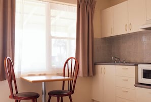 A kitchen with a window, two wooden chairs, a table, and a microwave.