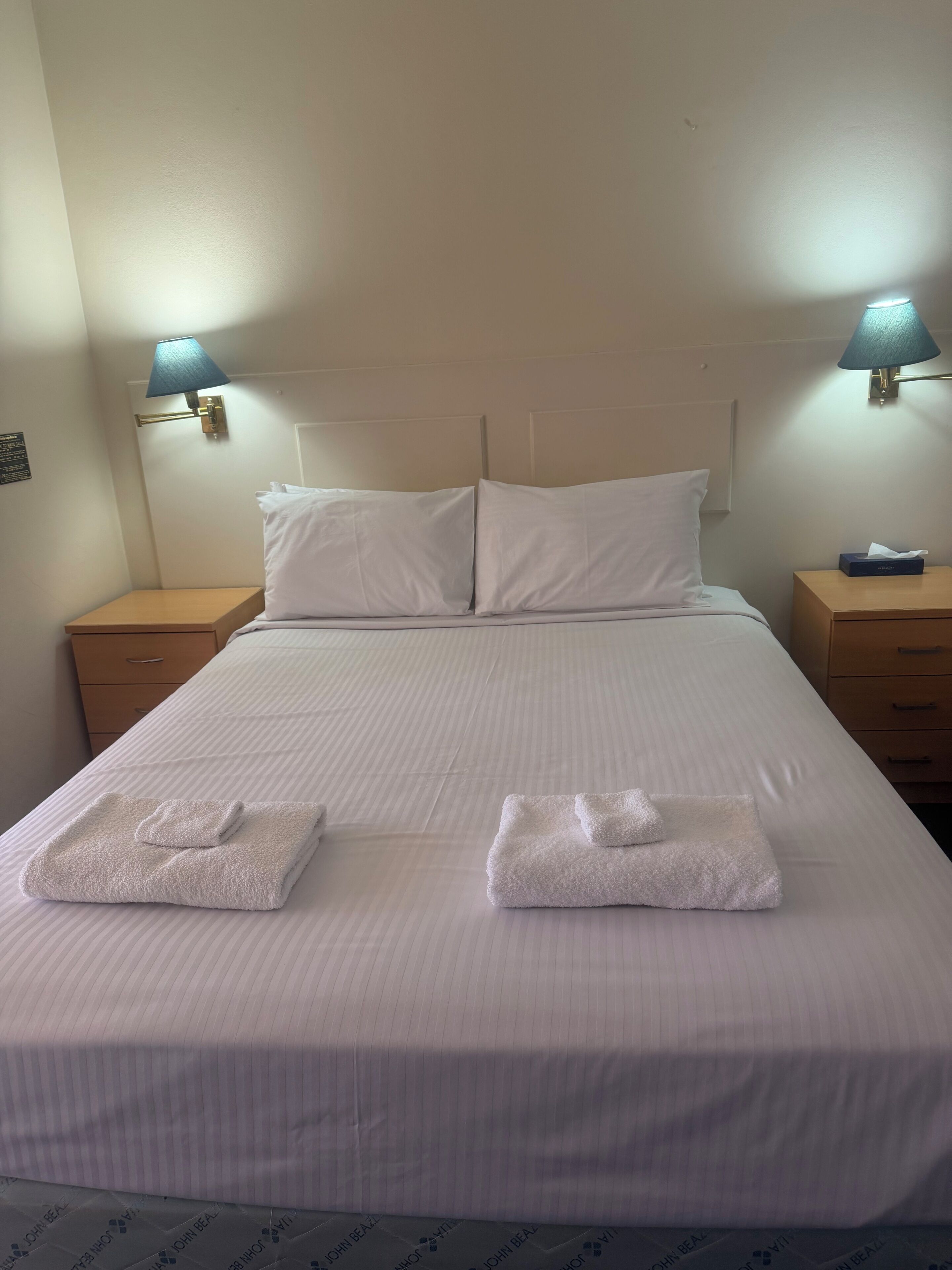 A hotel room with a bed, two nightstands, and two wall-mounted lamps.