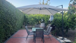 An outdoor patio with a table and chairs, a large umbrella, and a barbecue grill. - Cozy apartment with a view of Mount Etna, a spacious garden, and a relaxing atmosphere. No pets. (Aci Sant’Antonio)