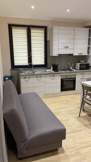 A modern kitchen with a built-in oven, microwave, and a dining area with a table and chairs. - Cozy apartment with a view of Mount Etna, a spacious garden, and a relaxing atmosphere. No pets. (Aci Sant’Antonio)