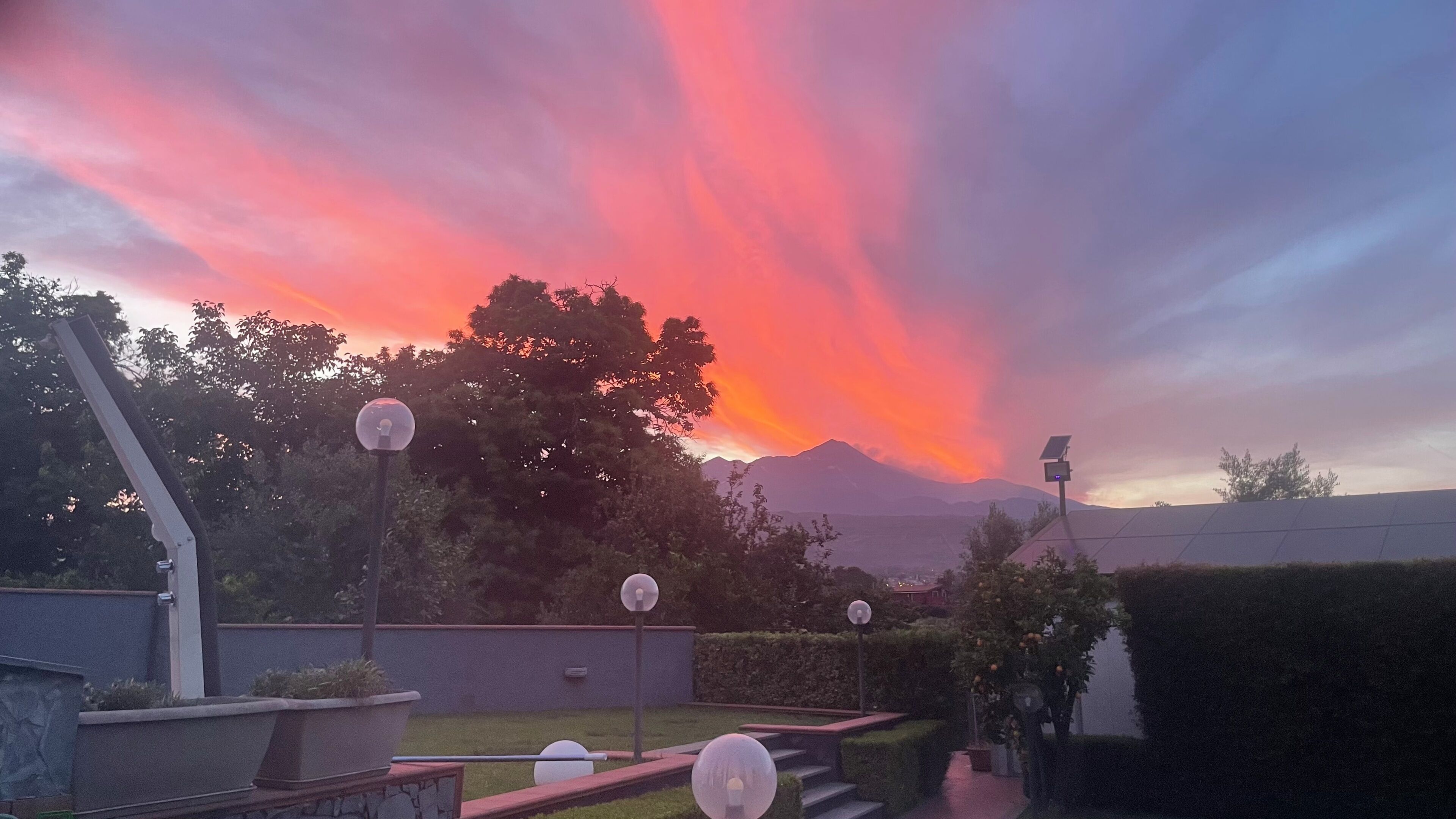 A garden with a street lamp, a hedge, and a mountain in the background.