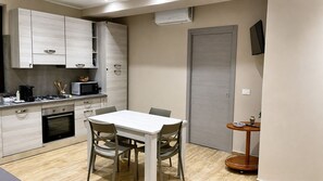 Een compacte keuken met een eethoek, inclusief kastjes, een magnetron, een fornuis en een tafel met stoelen.
