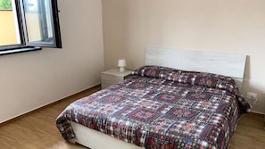 A bedroom with a bed, a nightstand, a lamp, and a window. - Cozy apartment with a view of Mount Etna, a spacious garden, and a relaxing atmosphere. No pets. (Aci Sant’Antonio)