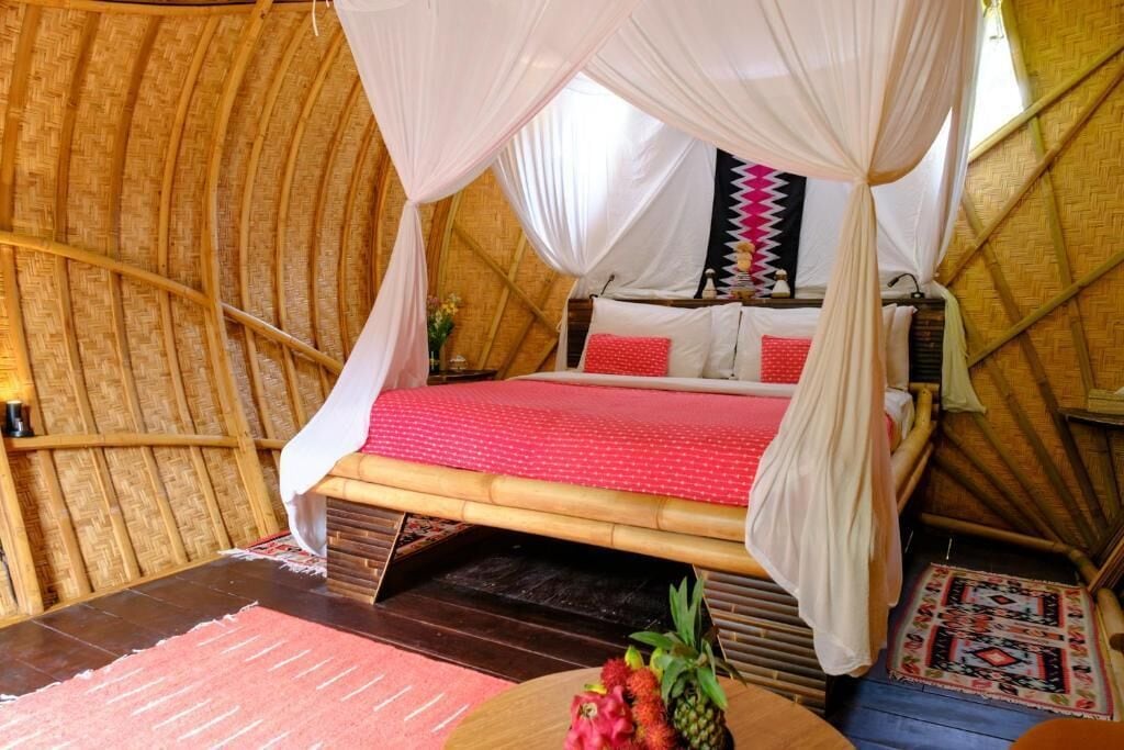 A room with a bed under a canopy, a wooden floor, and a small table with fruit.