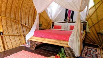 A room with a bed under a canopy, a wooden floor, and a small table with fruit.