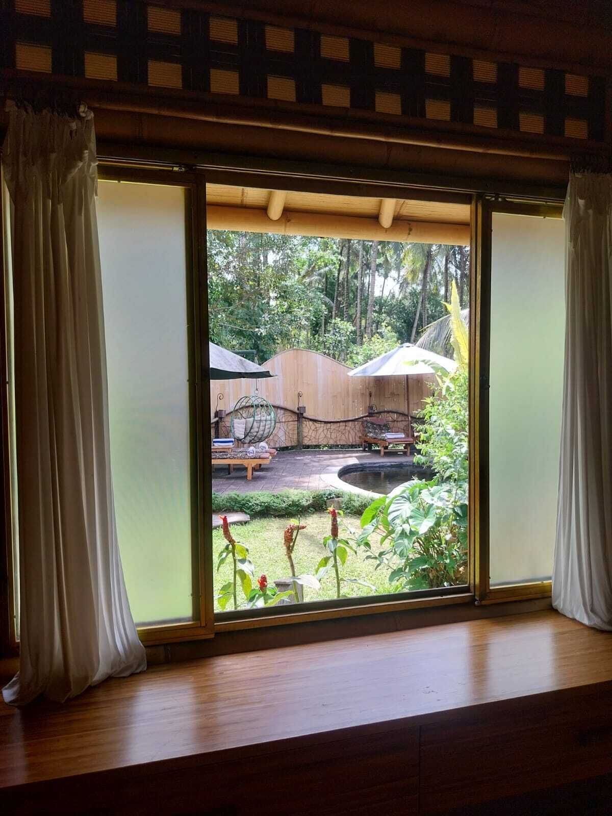 Una habitación con un gran ventanal corredera que da a un espacio exterior con terraza de madera, una hamaca y una piscina pequeña.