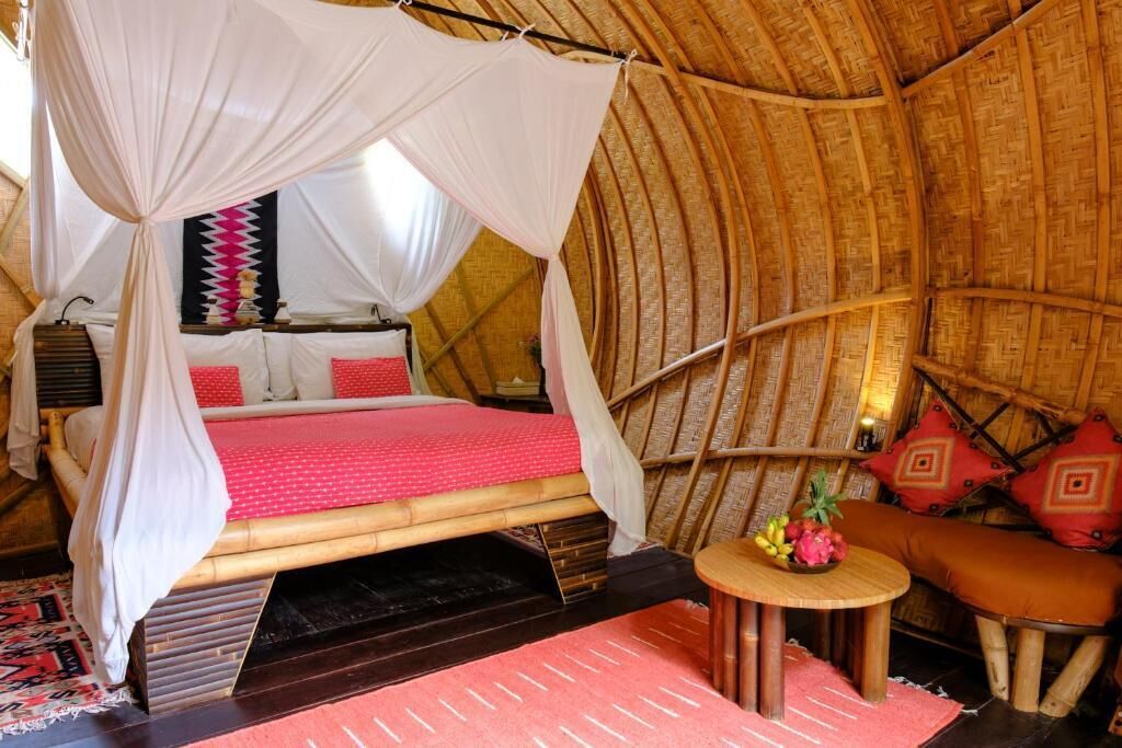 A room with a thatched roof, a bed with a canopy, a small round table, and a cushioned bench.