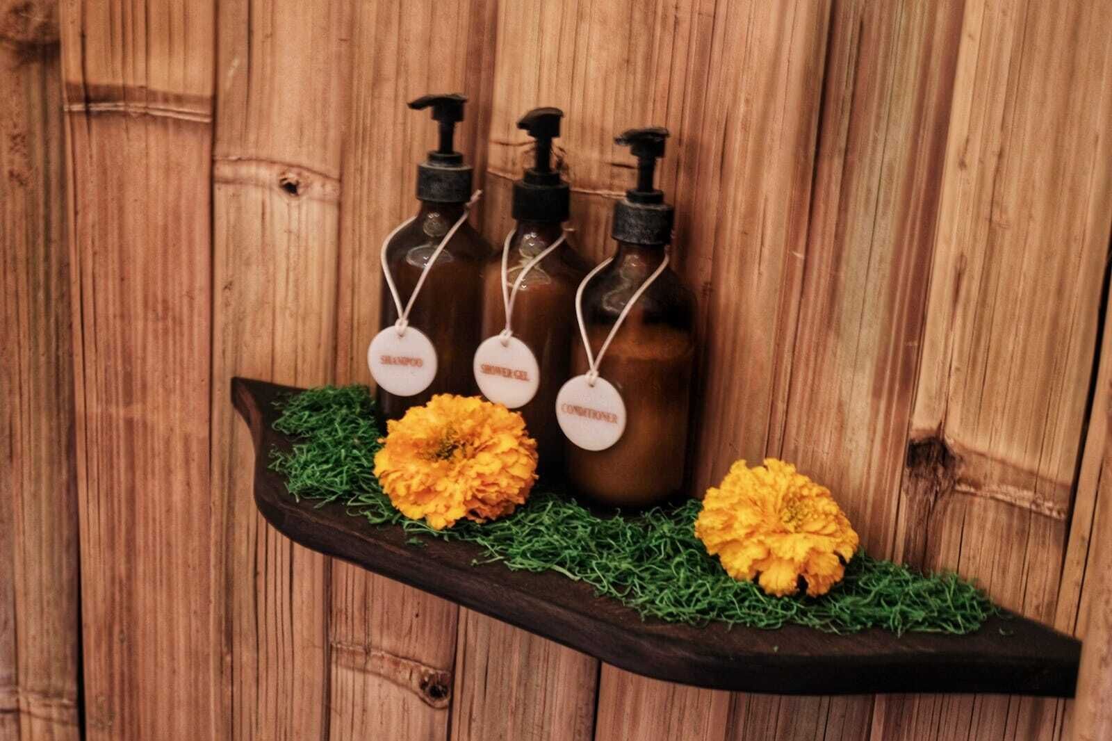 A wooden shelf with three bottles labeled 'SHAMPOO,' 'SHOWER GEL,' and 'CONDITIONER,' each with a pump dispenser.