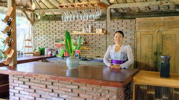 Zona de bar con mostrador de ladrillo, copas de vino colgantes y una variedad de botellas y plantas.