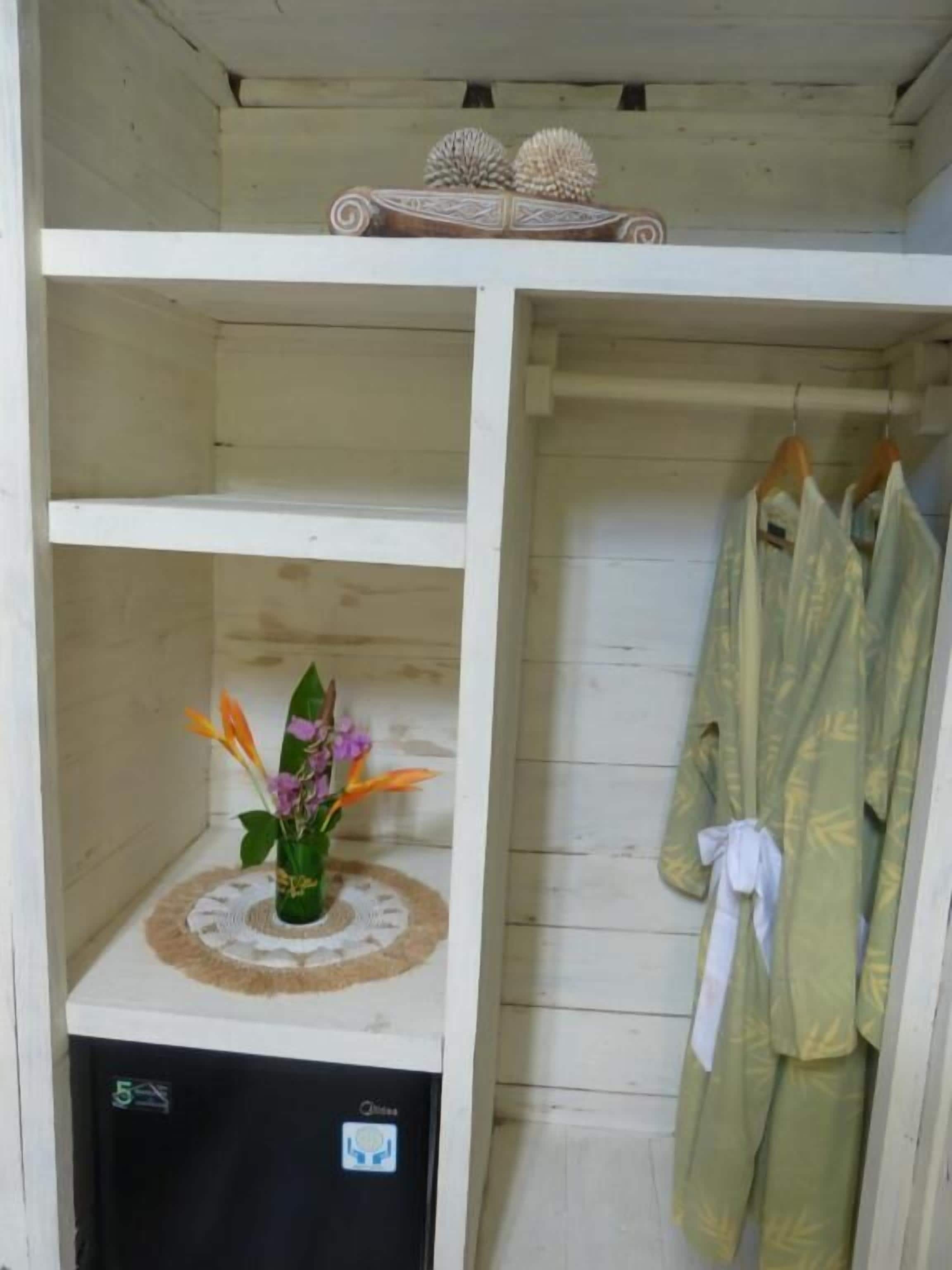 A room with a white wardrobe, a small refrigerator, and a robe hanging on the door.