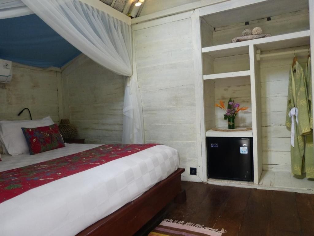 A bedroom with a bed, a bedside table, a nightstand, a wardrobe, and a small shelf with decorative items.
