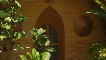 A wooden structure with a pointed arch doorway, surrounded by lush green foliage.