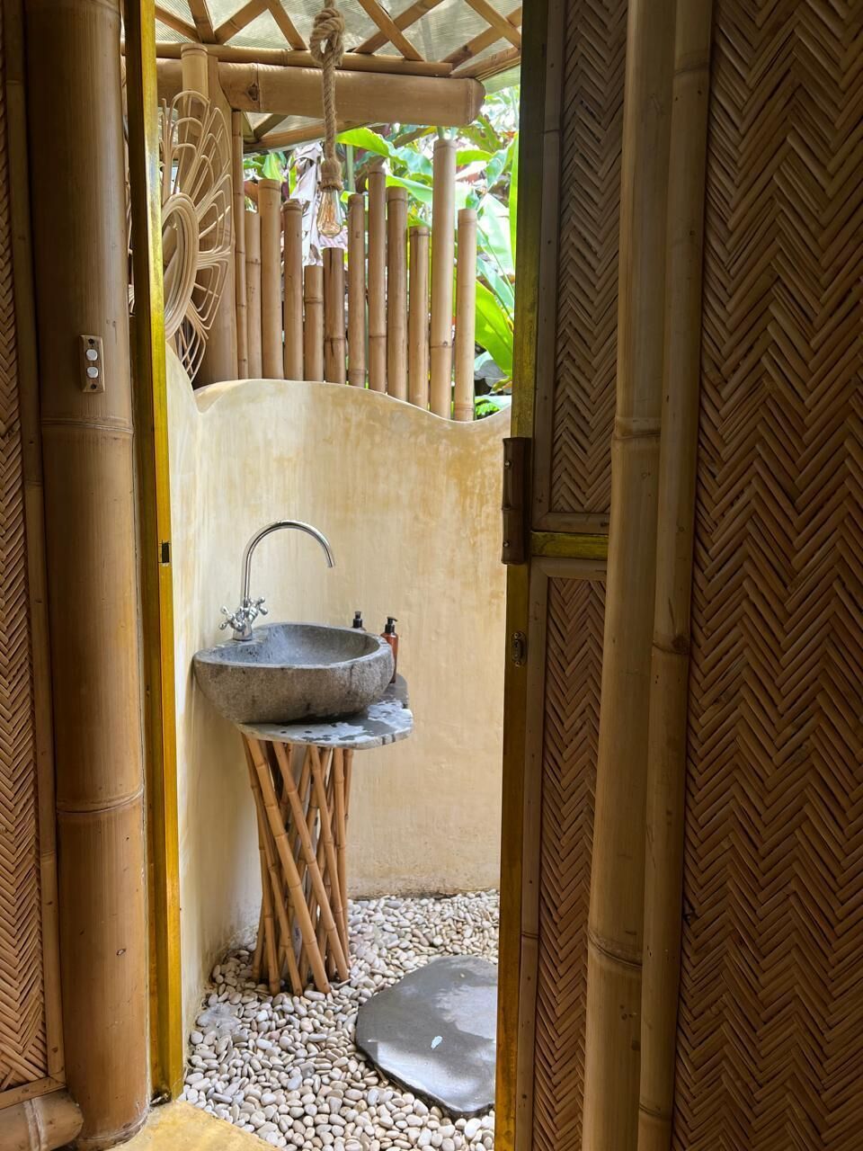 A bathroom with a stone sink, bamboo pillars, and a herringbone-patterned wall.