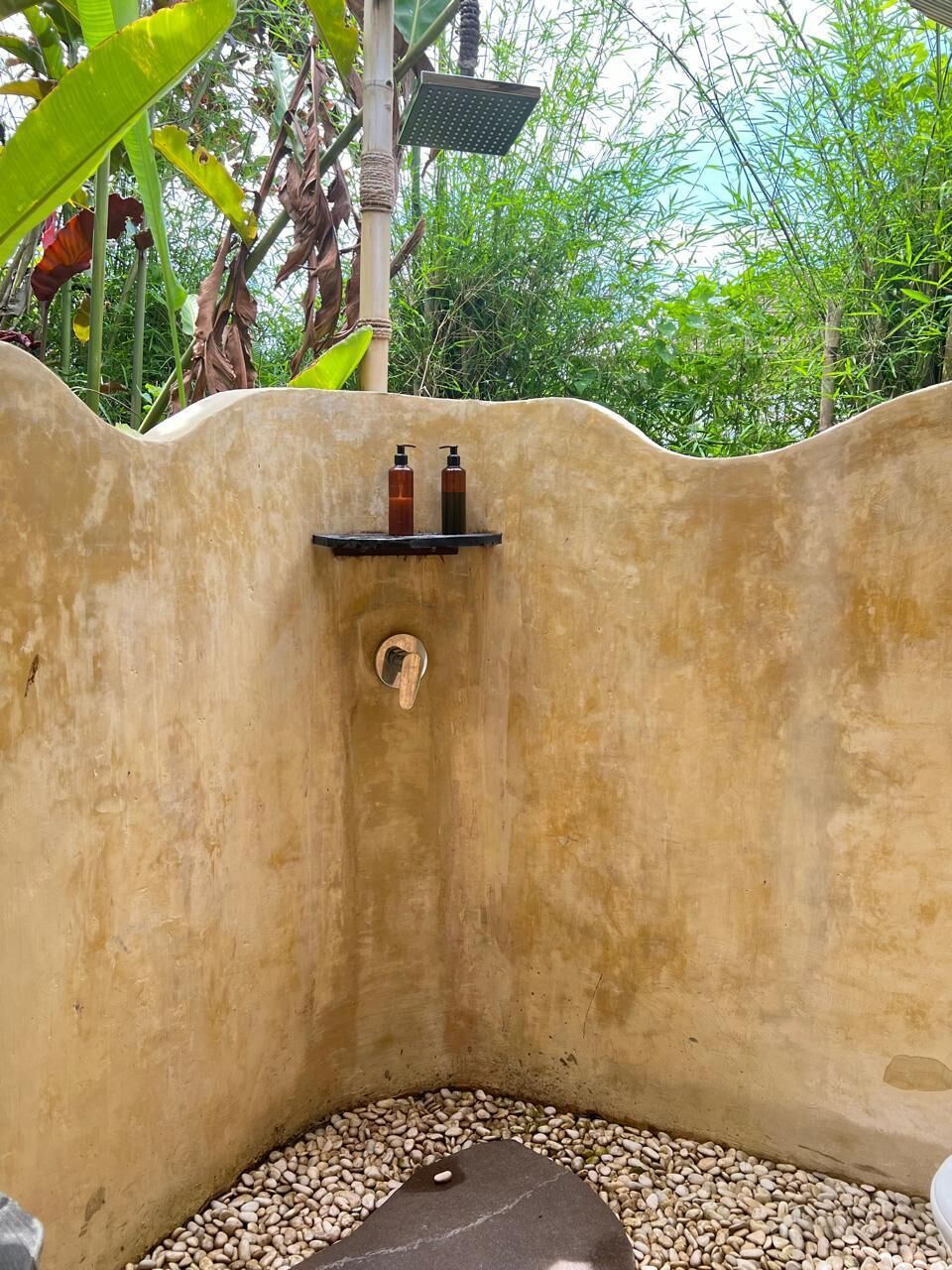 A small, enclosed shower area with a pebble floor, a shelf with toiletries, and a showerhead.