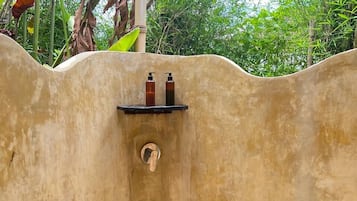 A small, enclosed shower area with a pebble floor, a shelf with toiletries, and a showerhead.