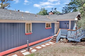 A house with a dark blue exterior, a red front door, and a wooden staircase leading to a porch. - Moon Palace 2170 (Big Bear City)