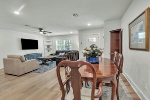A modern living room with a dining area, a flat-screen TV mounted on the wall, and a ceiling fan. - Harrington: 1 Min From Main Entrance to Texas A&M (College Station)