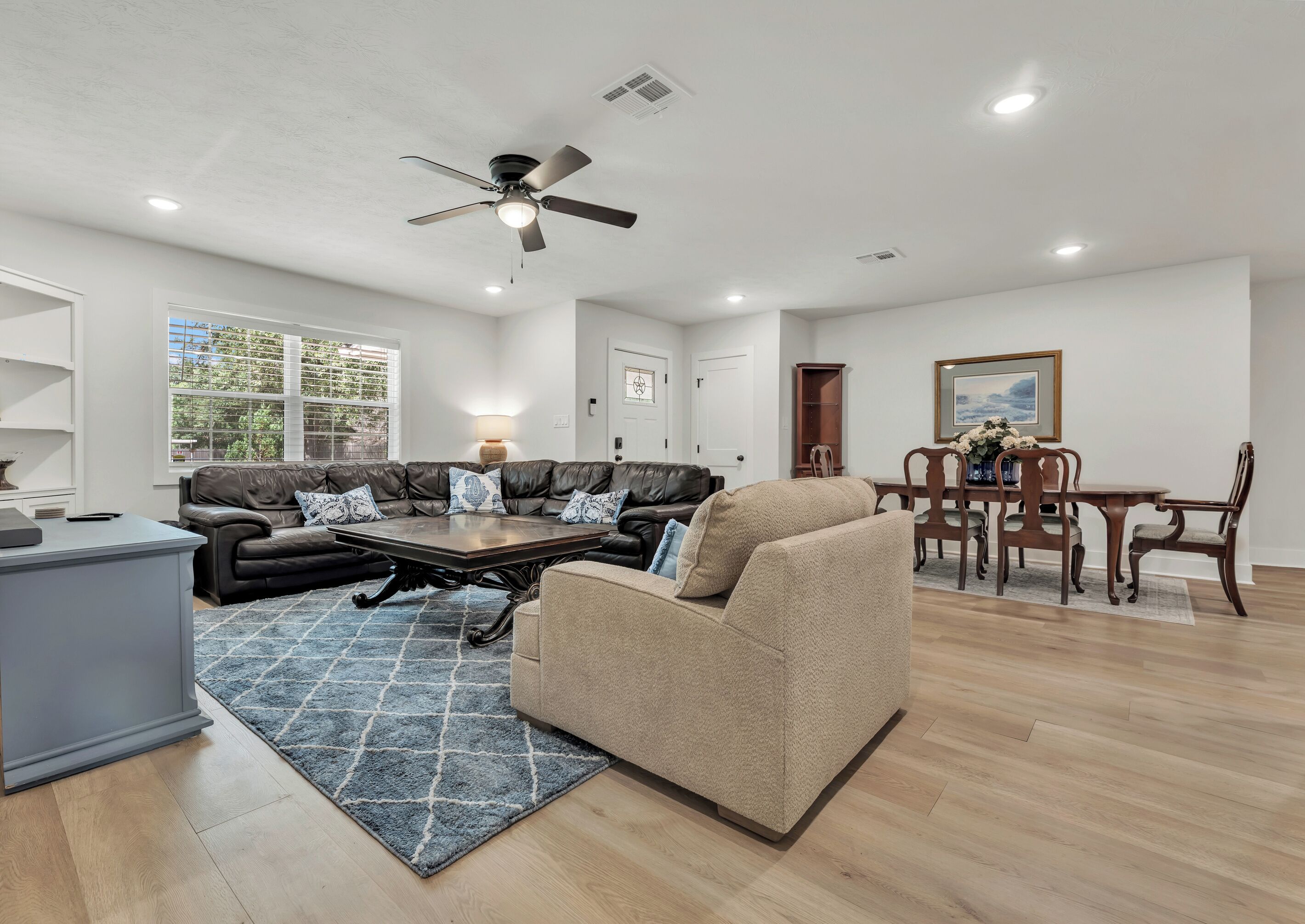 A spacious living room with a leather sofa, a beige armchair, a wooden coffee table, and a dining area with a wooden table and chairs.