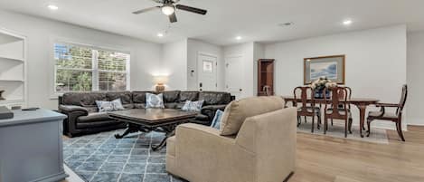 Amplia sala de estar con sofá de cuero, un sillón color beige, una mesa de centro de madera y una zona de comedor con mesa y sillas de madera.