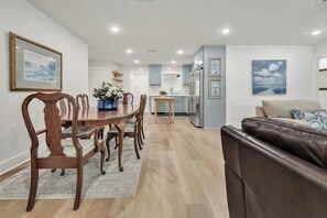 A modern living room with a brown leather sofa, a dining area with wooden chairs and a glass table, and a kitchen with light blue cabinets and a refrigerator. - Harrington: 1 Min From Main Entrance to Texas A&M (College Station)