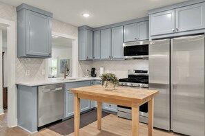 A modern kitchen with grey cabinets, stainless steel appliances, and a wooden table. - Harrington: 1 Min From Main Entrance to Texas A&M (College Station)