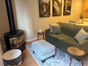 A cozy living room with a wood-burning stove, a green sofa, a patterned rug, and a small wooden table. - Enjoy your stay at our guest suite located in the Chilliwack Eastern Hillsides. (Chilliwack)