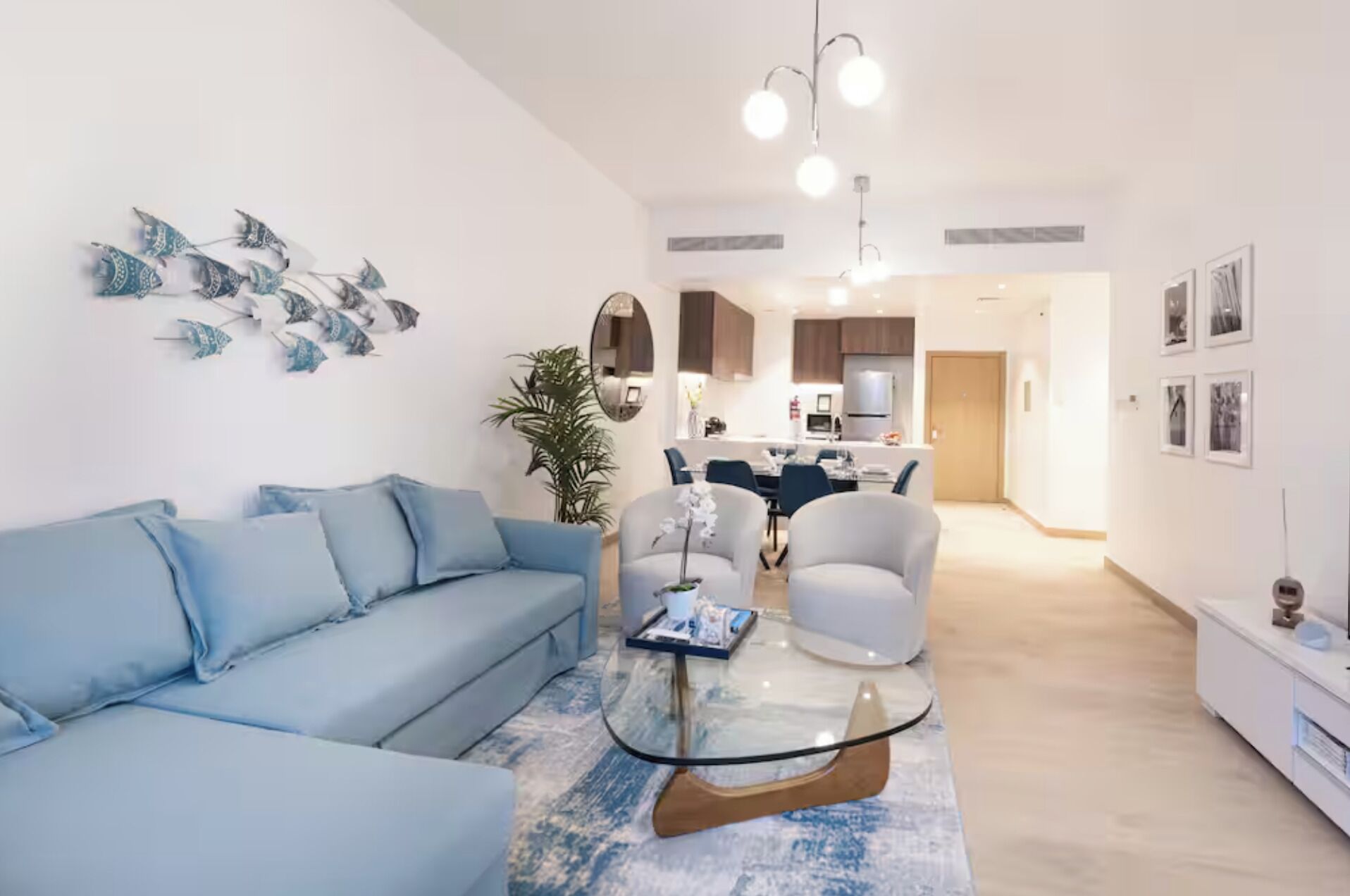 A modern living room with a sofa, a glass coffee table, and a dining area with chairs.