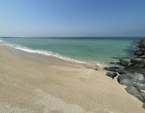 A beach with clear water, a sandy shore, and rocky outcrops. - bnbme - La Cote 3 - 2BR (Dubai)
