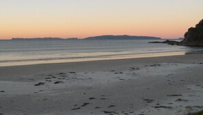 A beach with a calm sea, a clear sky, and distant landforms. - MATARANGI BACH Cosy 2 bedroom bach in a lush garden setting (Matarangi)