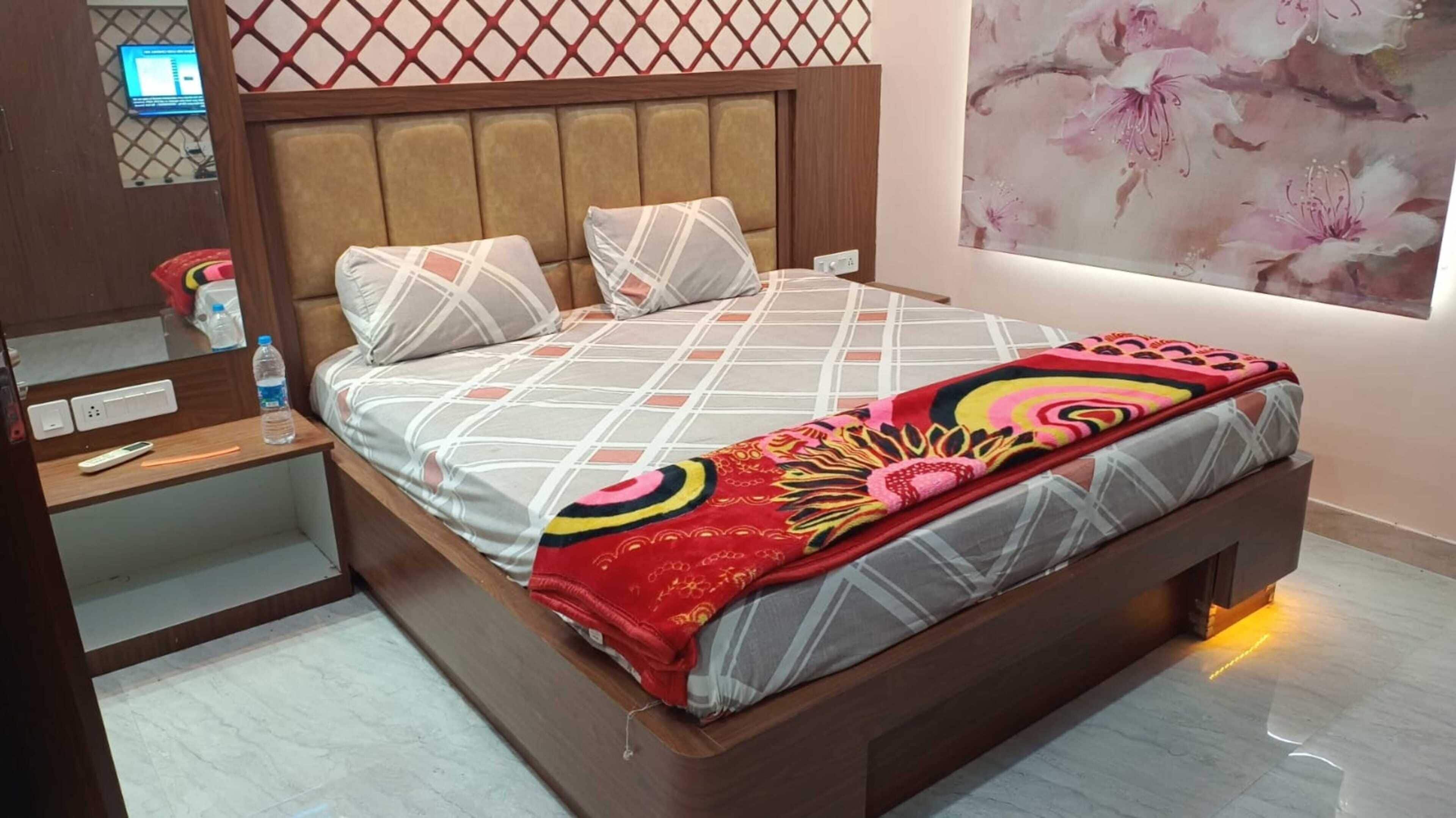 Una cama con cabecera, almohadas, una manta y una mesita de noche con una botella y un control remoto.