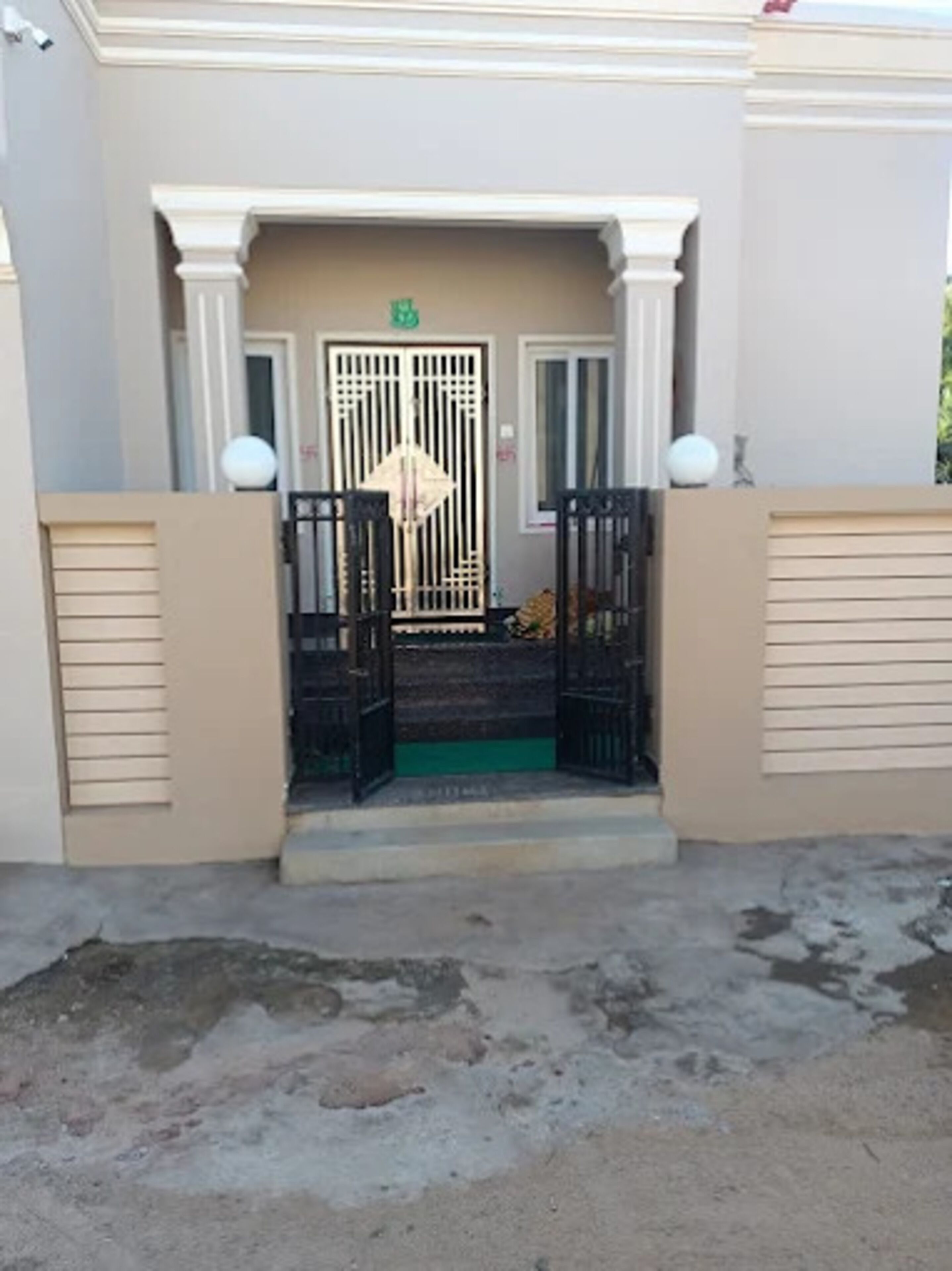 Una entrada de edificio con puerta enrejada, felpudo verde y un escalón que lleva a la puerta.