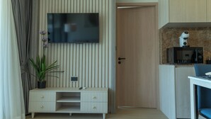 Ein modernes Zimmer mit einem flachbildfernseher an einer Holzwand, einem kleinen Schreibtisch mit Schubladen, einer Topfpflanze und einer Mikrowelle auf einer Arbeitsplatte.