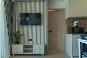 Ein modernes Zimmer mit einem flachbildfernseher an einer Holzwand, einem kleinen Schreibtisch mit Schubladen, einer Topfpflanze und einer Mikrowelle auf einer Arbeitsplatte.