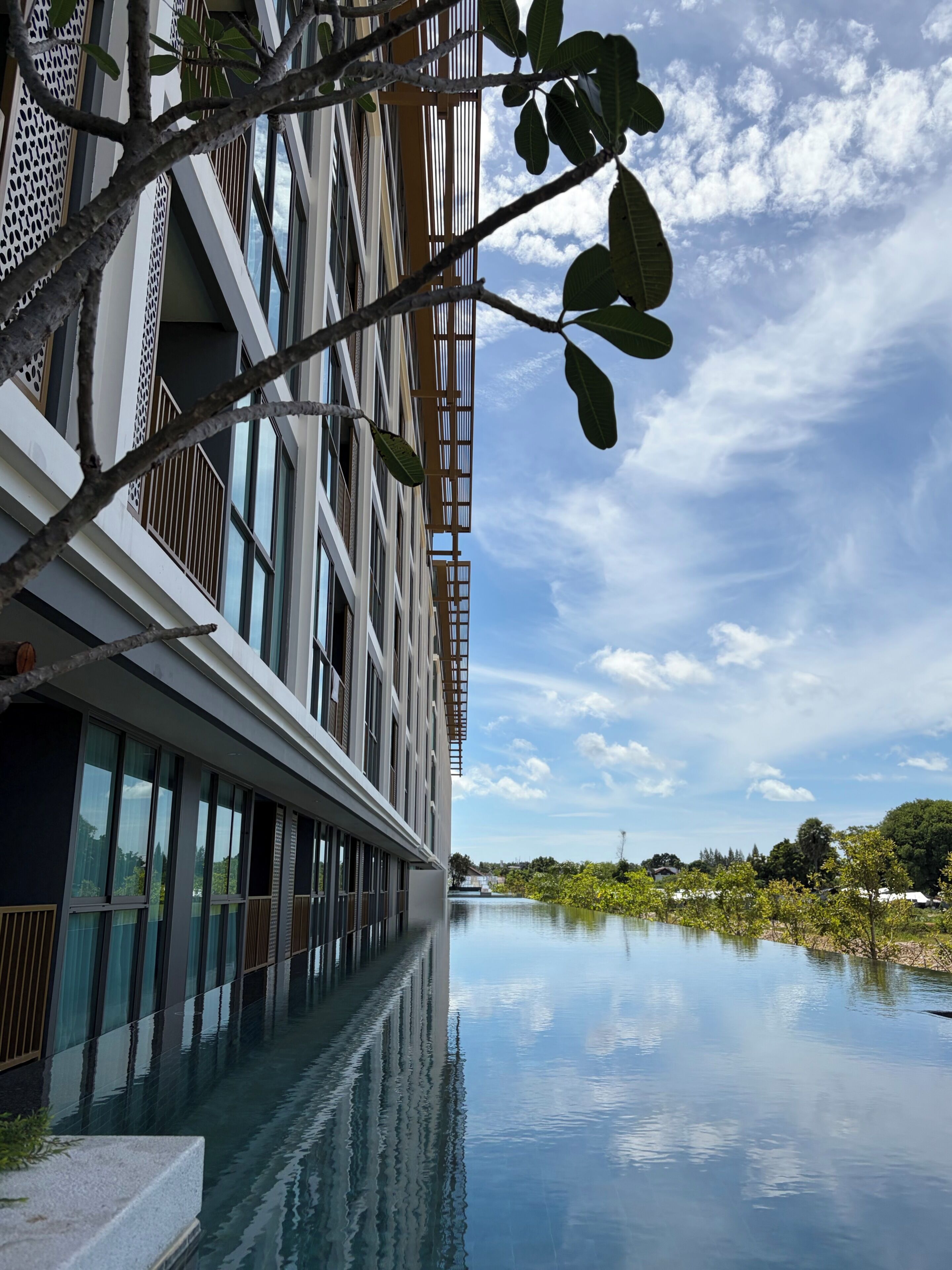 Un edificio moderno con una piscina reflectante, amplios ventanales y cielo despejado.