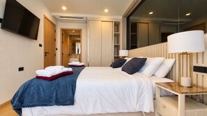 Habitación de hotel con cama, lámparas de noche, televisor de pantalla plana y baño a la vista a través de una puerta abierta.