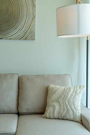 Ein beiges Sofa mit einem gemusterten Zierkissen und einem an der Wand hängenden abstrakten Kunstwerk.