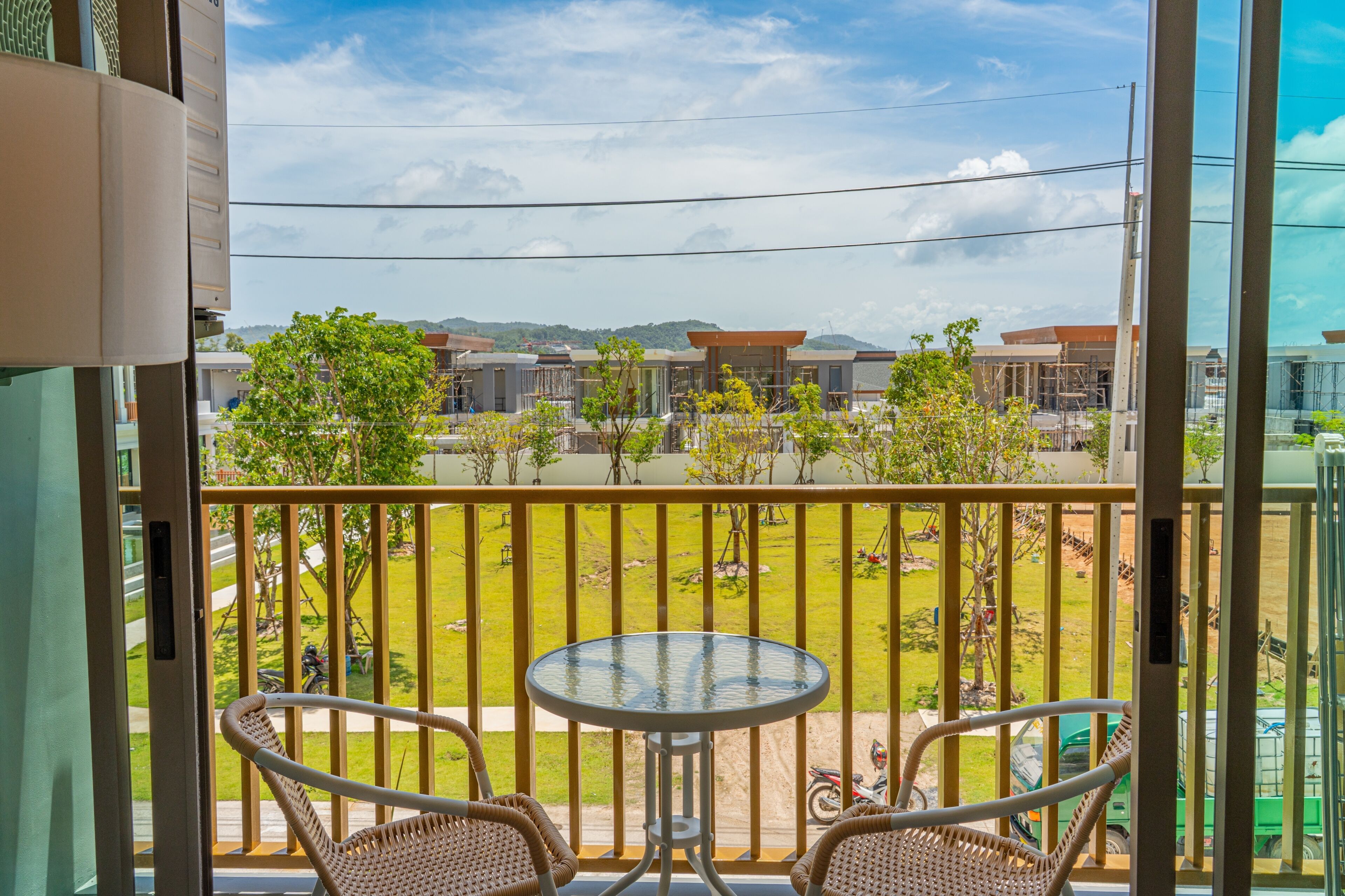 Un balcone con due sedie in vimini e un tavolino, affacciato su una zona verde con alberi e edifici sullo sfondo.