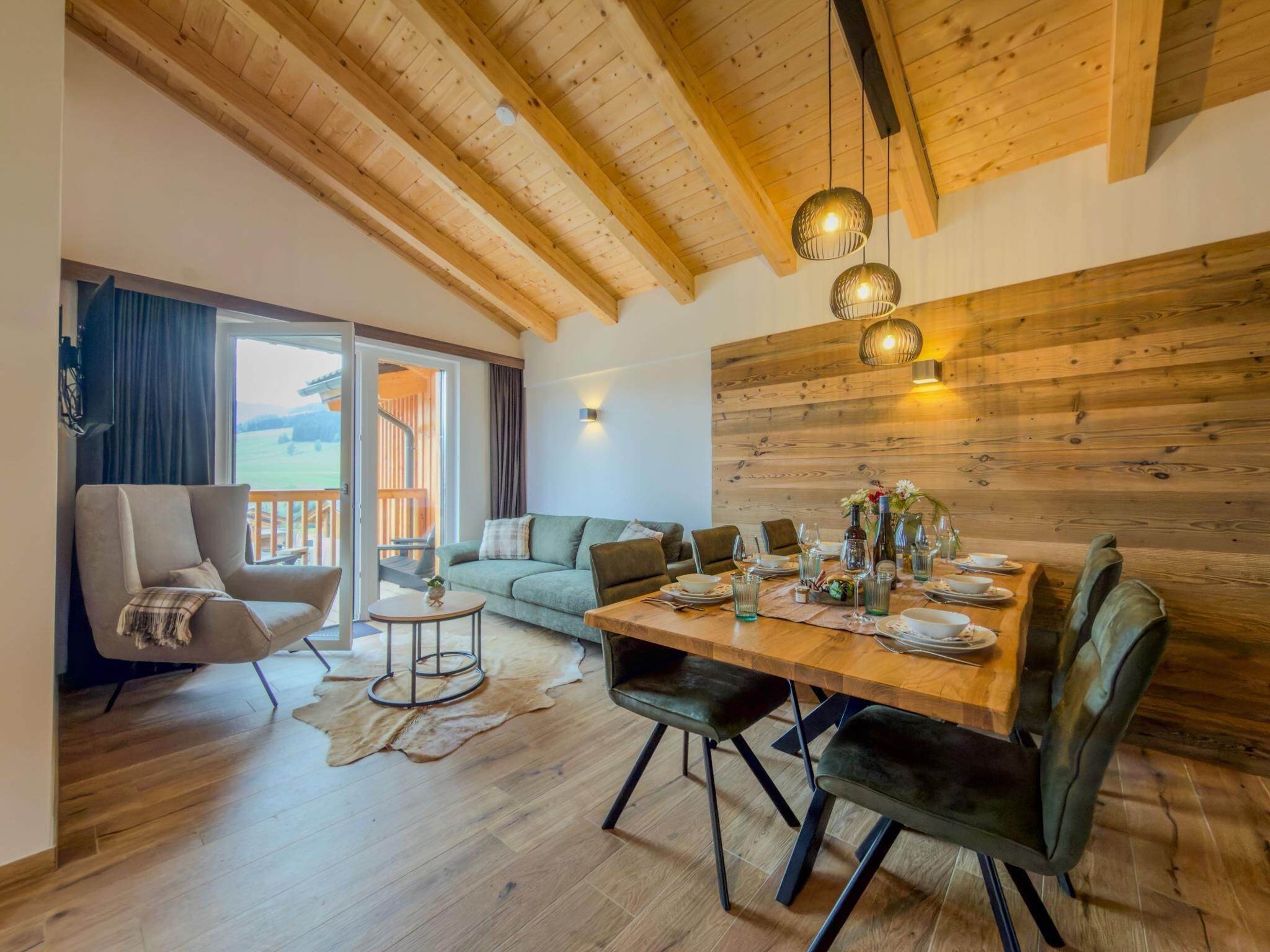 Un amplio salón con techo de madera, una mesa de comedor preparada para cuatro personas, un sofá y una silla.